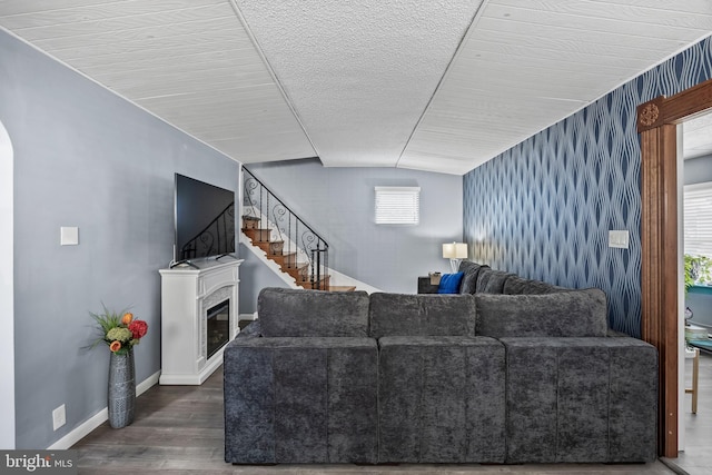 living room with a glass covered fireplace, wood finished floors, stairway, baseboards, and lofted ceiling