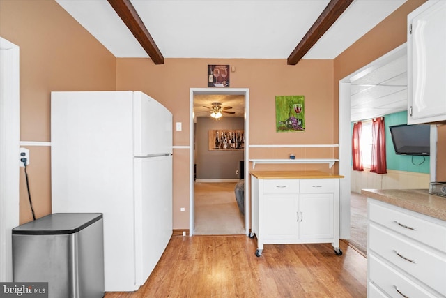 kitchen with light countertops, beam ceiling, light wood-style flooring, freestanding refrigerator, and white cabinets