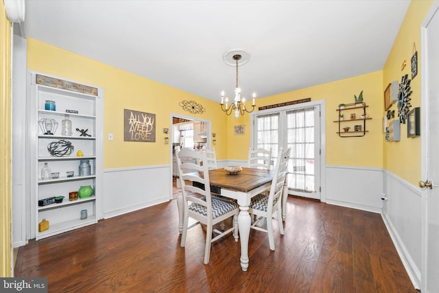 dining room featuring dark wood-style floors, wainscoting, built in shelves, and an inviting chandelier