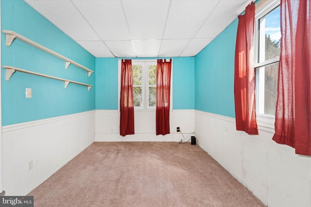 empty room with carpet flooring, wainscoting, and a drop ceiling