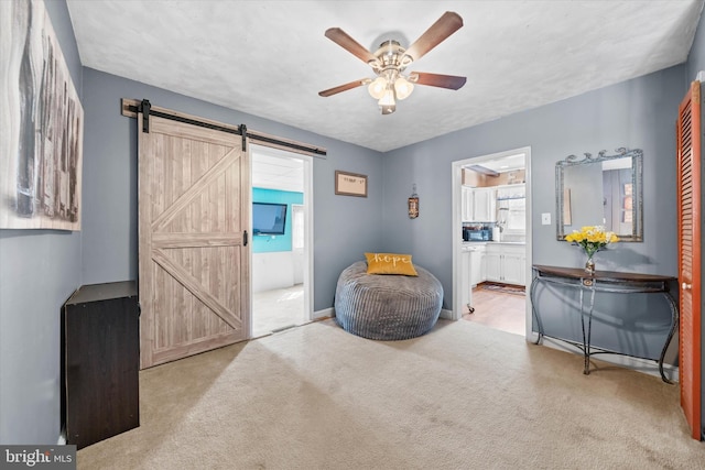 sitting room featuring a barn door, baseboards, carpet floors, and ceiling fan