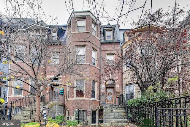 view of front of house with brick siding, mansard roof, fence, and a high end roof