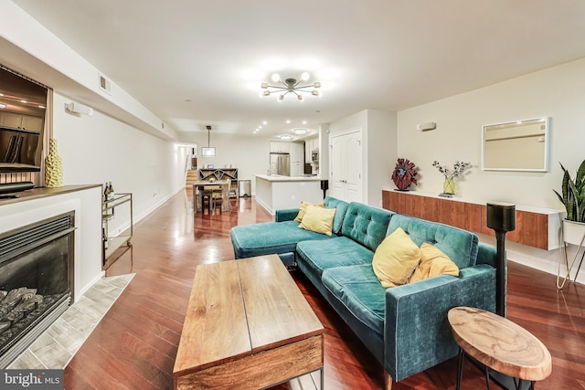 living area with a fireplace with flush hearth, visible vents, baseboards, and wood finished floors