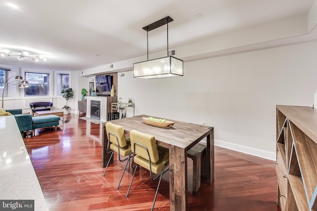 dining space with dark wood-type flooring, baseboards, visible vents, and a fireplace with flush hearth