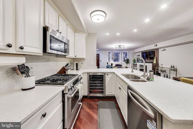 kitchen featuring dark wood finished floors, stainless steel appliances, white cabinetry, a sink, and beverage cooler