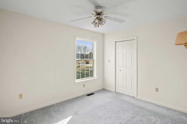 unfurnished bedroom featuring visible vents, baseboards, light colored carpet, a closet, and a ceiling fan