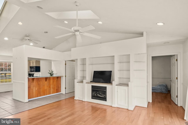 unfurnished living room featuring light wood-style flooring, a ceiling fan, recessed lighting, vaulted ceiling with skylight, and a fireplace