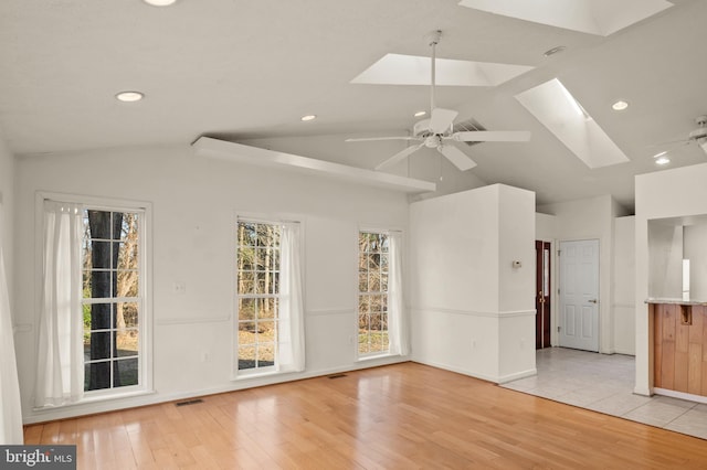 empty room featuring light wood-type flooring, lofted ceiling with skylight, visible vents, baseboards, and ceiling fan