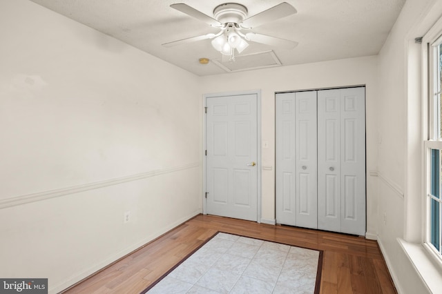 unfurnished bedroom featuring a closet, attic access, ceiling fan, and wood finished floors