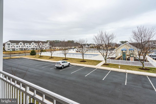 uncovered parking lot featuring fence, playground community, and a residential view