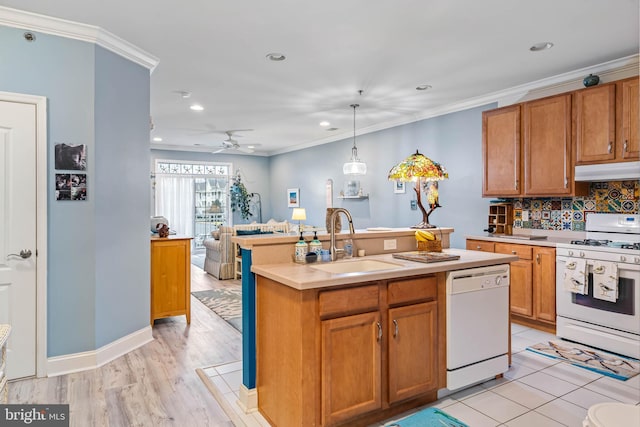 kitchen with white appliances, a sink, light countertops, under cabinet range hood, and crown molding