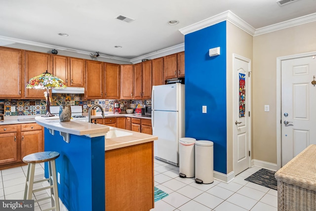 kitchen with under cabinet range hood, light countertops, freestanding refrigerator, and a sink