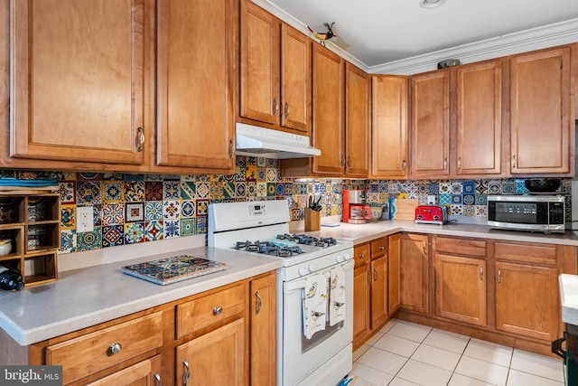 kitchen featuring stainless steel microwave, under cabinet range hood, white gas range, decorative backsplash, and light tile patterned flooring