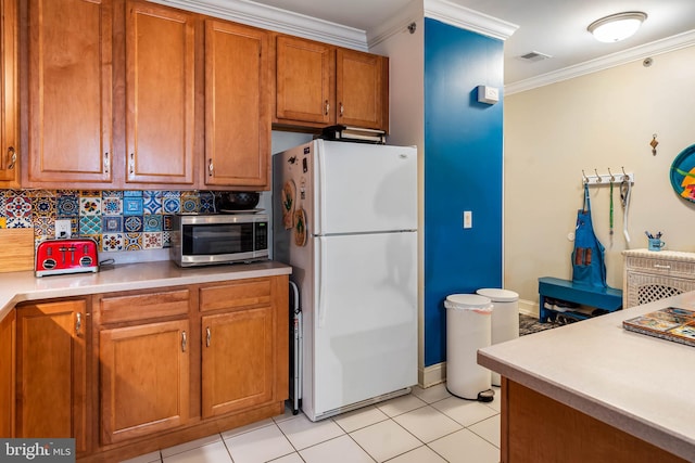 kitchen with visible vents, brown cabinets, ornamental molding, stainless steel microwave, and freestanding refrigerator