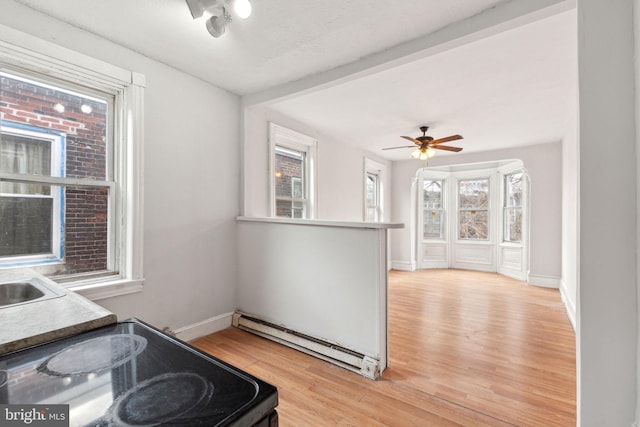 kitchen with electric range oven, a baseboard heating unit, light wood-style floors, a ceiling fan, and baseboards