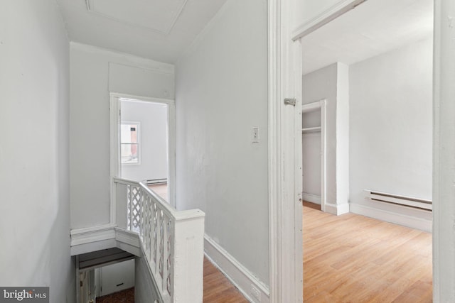 hallway with a baseboard heating unit, wood finished floors, an upstairs landing, and baseboards