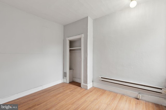 unfurnished bedroom with a baseboard radiator, a closet, baseboards, and wood finished floors