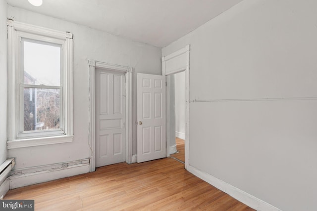 unfurnished bedroom featuring light wood-style floors, a baseboard radiator, and baseboards