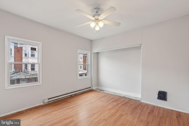 spare room featuring a baseboard heating unit, light wood-style floors, baseboards, and ceiling fan