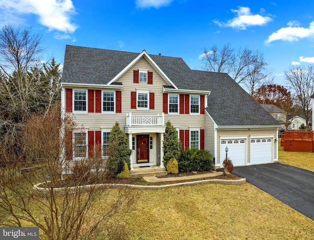 colonial house with a garage, a shingled roof, a front lawn, and aphalt driveway