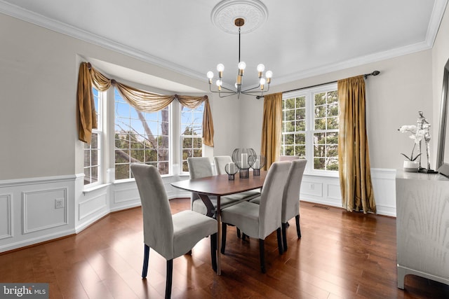 dining room featuring dark wood-style flooring, visible vents, a decorative wall, ornamental molding, and a chandelier