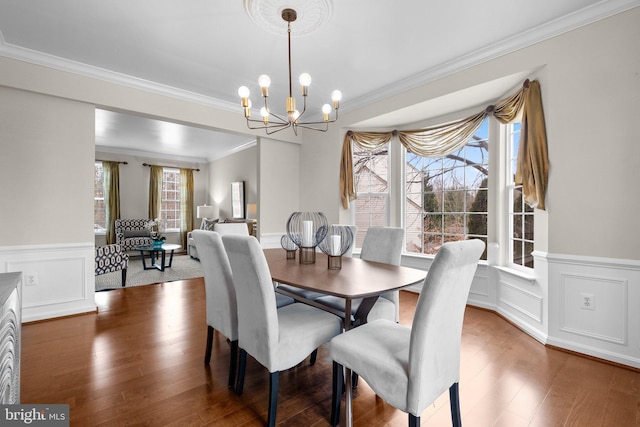 dining space with a chandelier, a decorative wall, wood finished floors, and crown molding