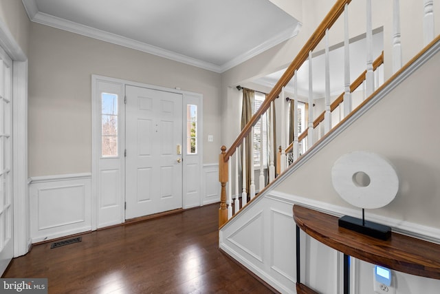 foyer entrance featuring dark wood-style floors, a wainscoted wall, visible vents, and ornamental molding