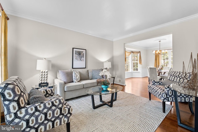 living room featuring a chandelier, visible vents, ornamental molding, and wood finished floors