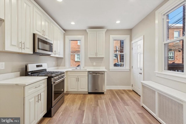 kitchen featuring stainless steel appliances, a sink, light countertops, light wood-type flooring, and radiator heating unit