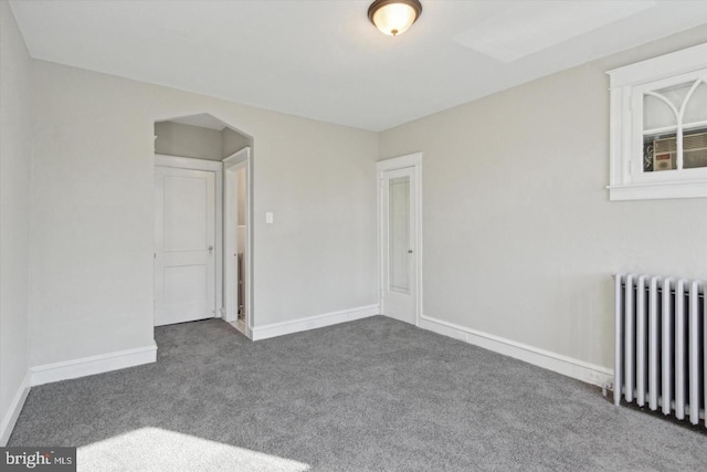 spare room with carpet, radiator, arched walkways, and baseboards