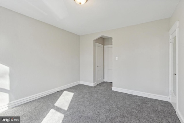 unfurnished bedroom with arched walkways, dark colored carpet, and baseboards