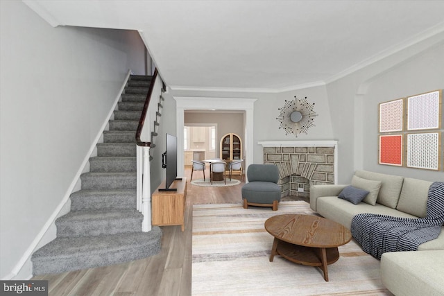 living area with stairway, light wood-style floors, ornamental molding, a brick fireplace, and baseboards