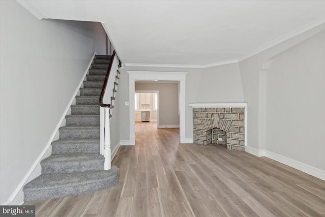 unfurnished living room with ornamental molding, a fireplace, baseboards, and wood finished floors