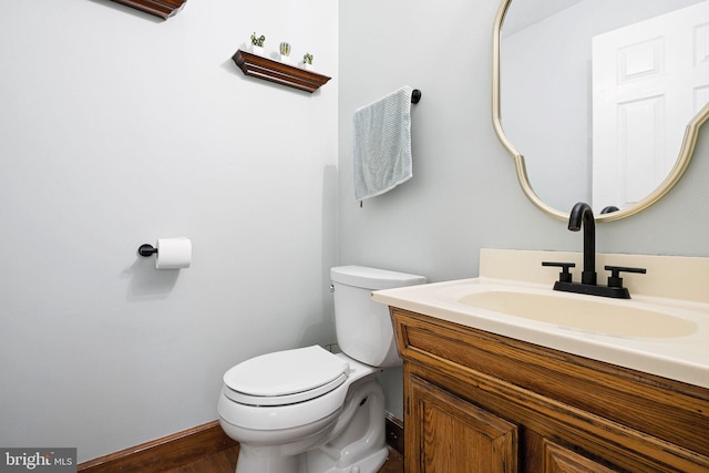 half bathroom with baseboards, vanity, toilet, and wood finished floors