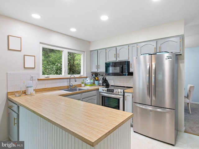 kitchen with tasteful backsplash, a peninsula, stainless steel appliances, light countertops, and a sink