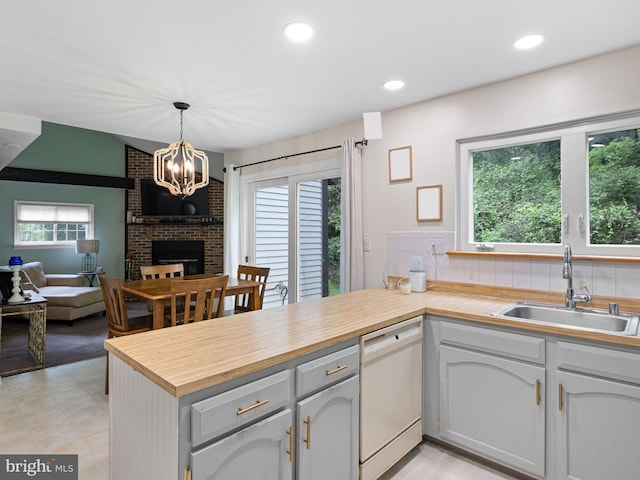 kitchen with white dishwasher, a peninsula, a fireplace, a sink, and plenty of natural light