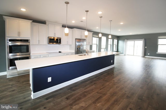 kitchen with a spacious island, backsplash, dark wood finished floors, light countertops, and appliances with stainless steel finishes