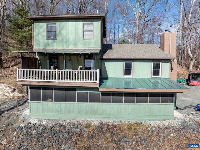 back of property featuring roof with shingles, a sunroom, and a chimney