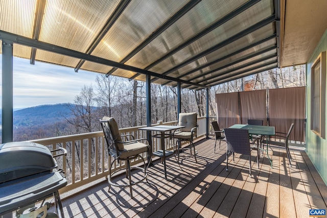 wooden deck with a mountain view, outdoor dining area, area for grilling, and a wooded view