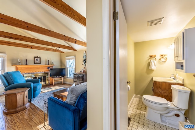 bathroom featuring visible vents, a sink, a glass covered fireplace, beamed ceiling, and toilet