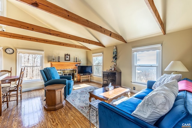 living area featuring a fireplace, vaulted ceiling with beams, baseboards, and wood finished floors