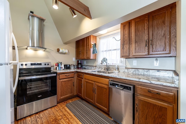 kitchen with light wood-style flooring, appliances with stainless steel finishes, brown cabinetry, wall chimney exhaust hood, and a sink