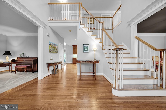 foyer with ornamental molding, a high ceiling, baseboards, and wood finished floors