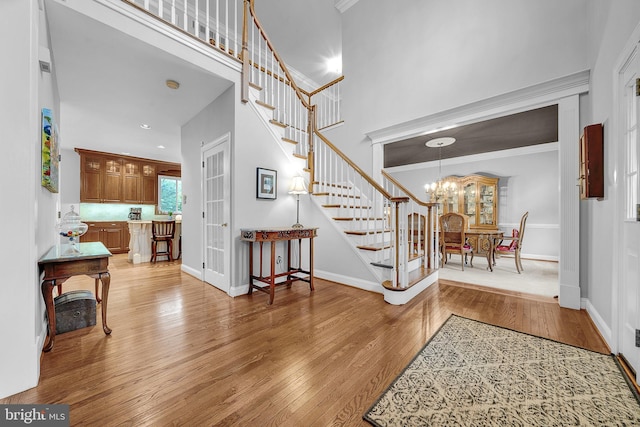 entryway featuring a chandelier, baseboards, ornamental molding, stairway, and light wood finished floors