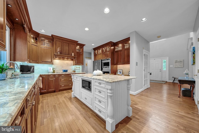 kitchen with decorative backsplash, appliances with stainless steel finishes, glass insert cabinets, light wood-type flooring, and a sink