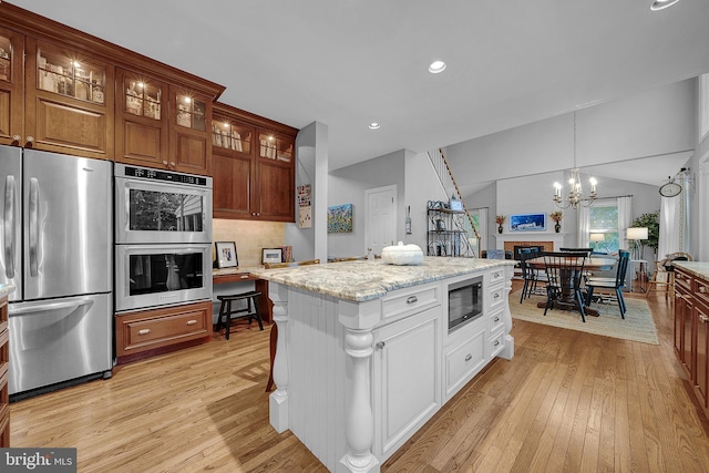 kitchen featuring light wood-style flooring, glass insert cabinets, appliances with stainless steel finishes, light stone counters, and vaulted ceiling