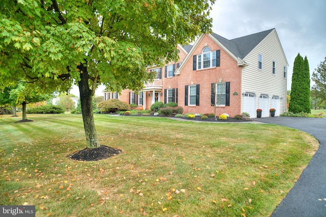 view of front of house featuring brick siding, a front lawn, an attached garage, and aphalt driveway