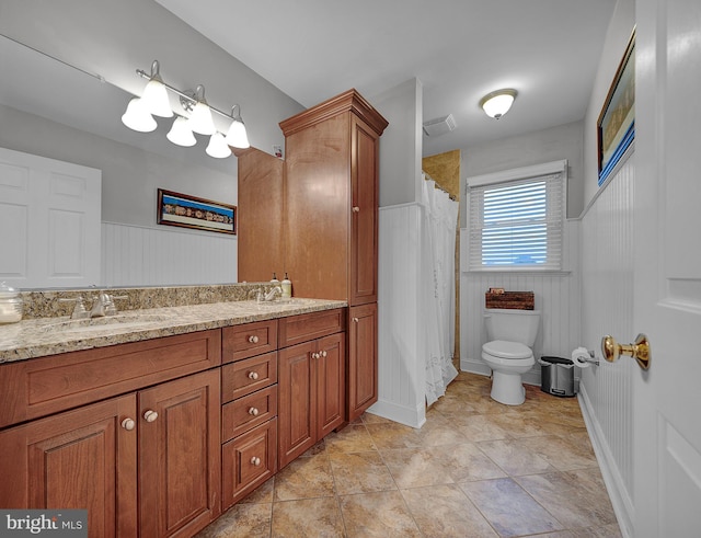 full bathroom featuring a wainscoted wall, double vanity, a sink, and toilet