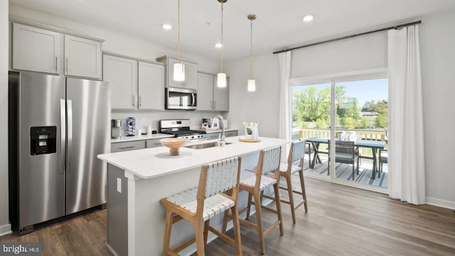 kitchen with dark wood-type flooring, a kitchen island with sink, stainless steel appliances, light countertops, and a sink