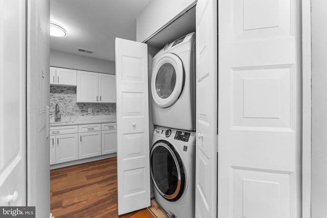 clothes washing area with stacked washer and dryer, visible vents, a sink, wood finished floors, and laundry area